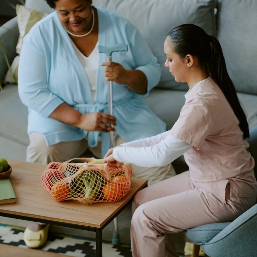 Caring nurse helping mature African American female patient with food delivery